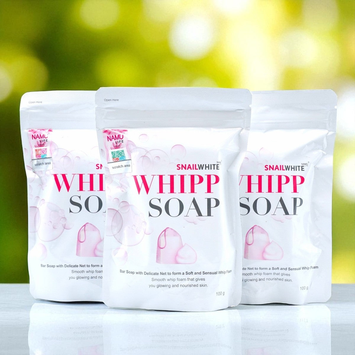 Three packs of authentic Namu Life Snail White Whipp Soap standing on a reflective surface with a soft, natural bokeh background.